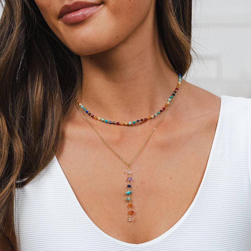 Model wearing 7 Chakras Healing Necklace layered with beaded choker, showcasing colorful raw gemstones on a gold chain for chakra balancing.