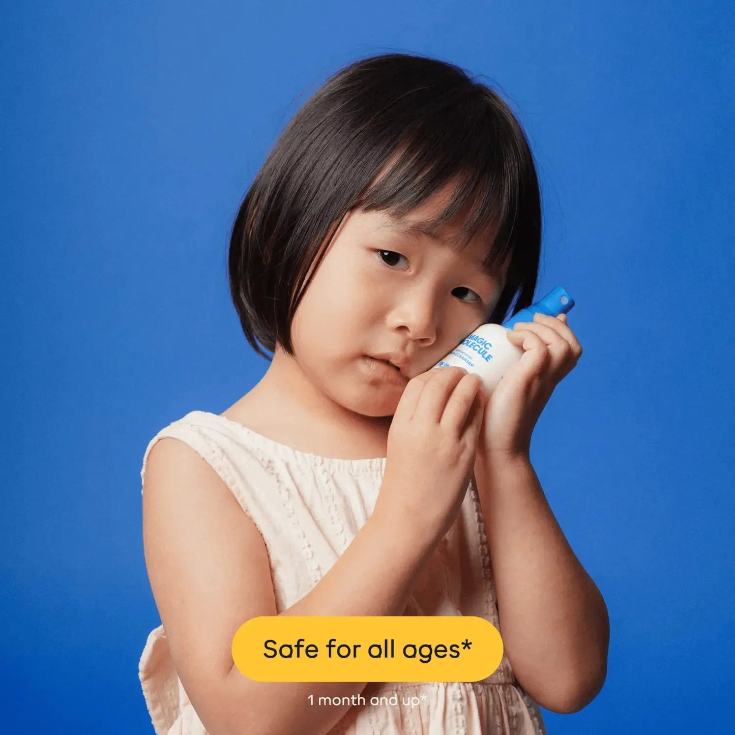 Young girl holding Magic Molecule Hypochlorous Acid Spray Mini against blue background. Gentle skin care spray safe for all ages, 1 month and up.