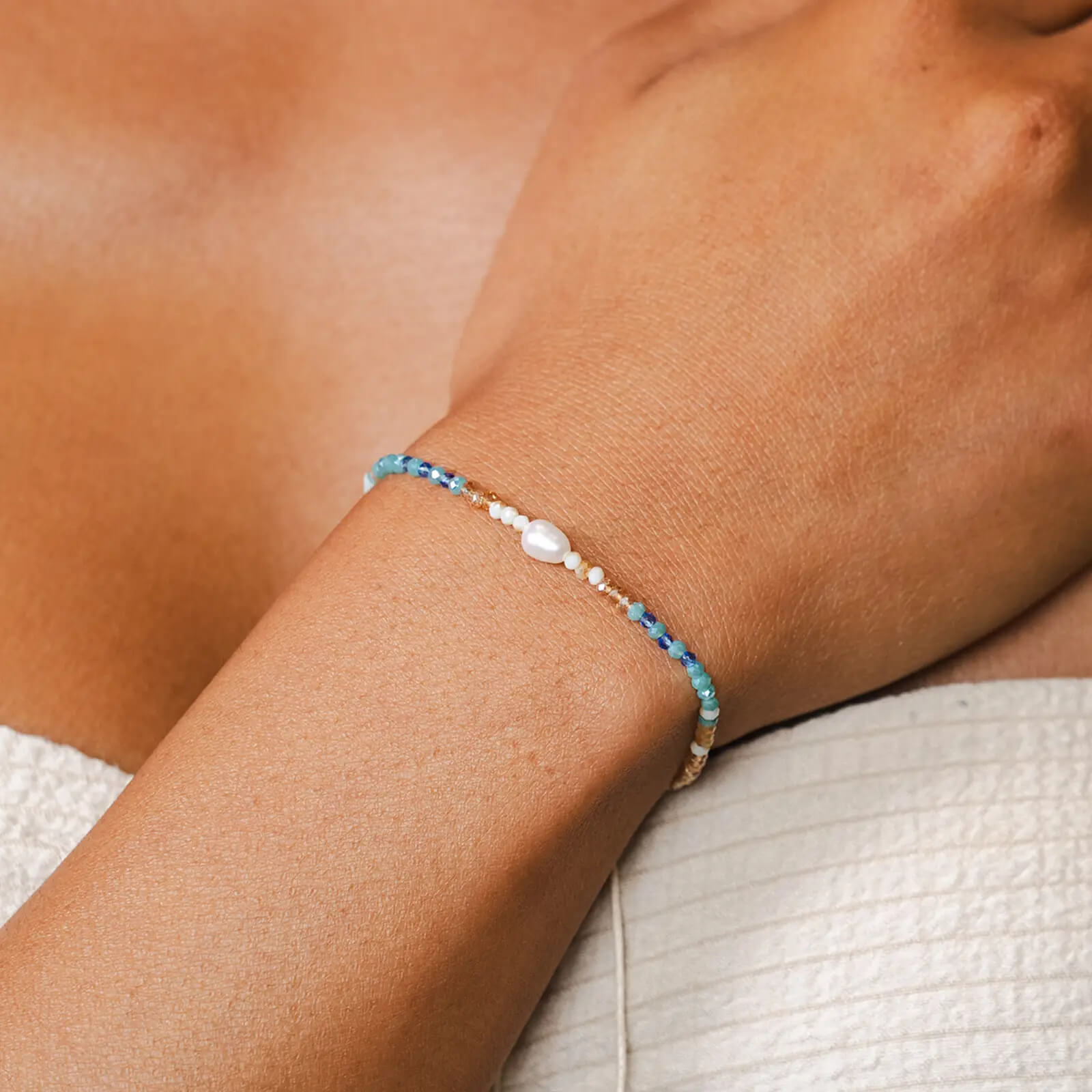 a wrist wearing the lotus and luna make waves goddess bracelet with freshwater pearl surrounded by blue, teal and gold crystals.