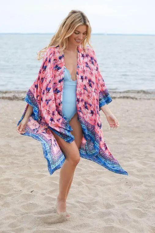 a woman is walking on the beach wearing a pink and blue cover up