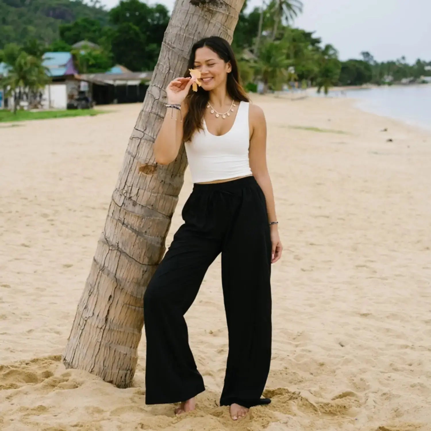 Black wide leg pants with pockets and a high-rise drawstring waist, styled with a white tank top on a beach. Comfortable boho lounge pants for casual wear.
