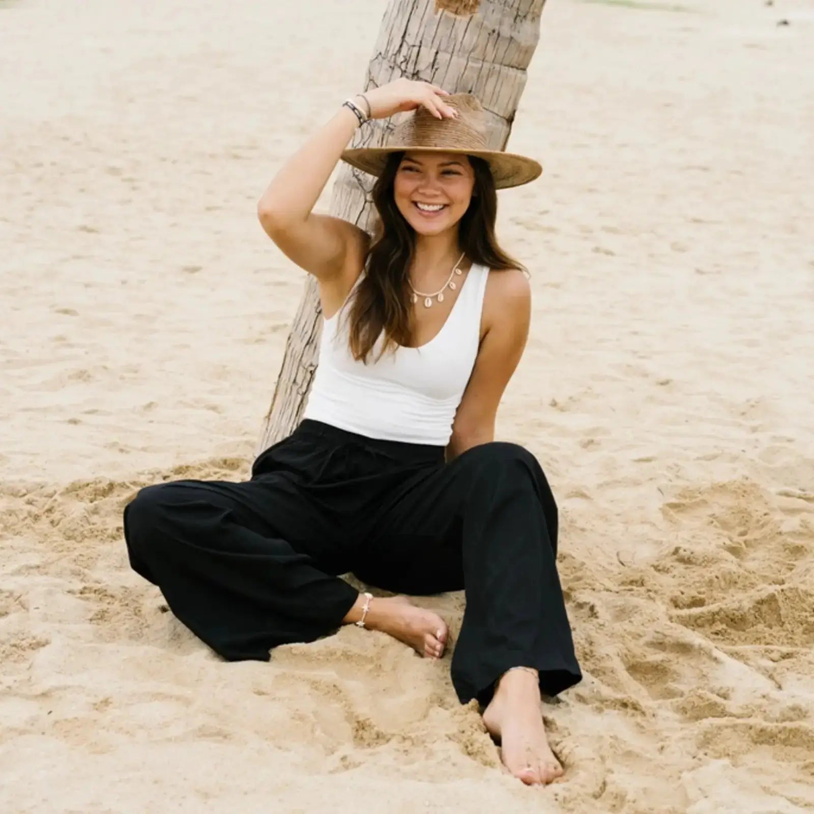 Black wide leg pants with pockets and a high-rise drawstring waist, styled with a white tank top on a beach. Relaxed fit boho lounge pants for casual wear.
