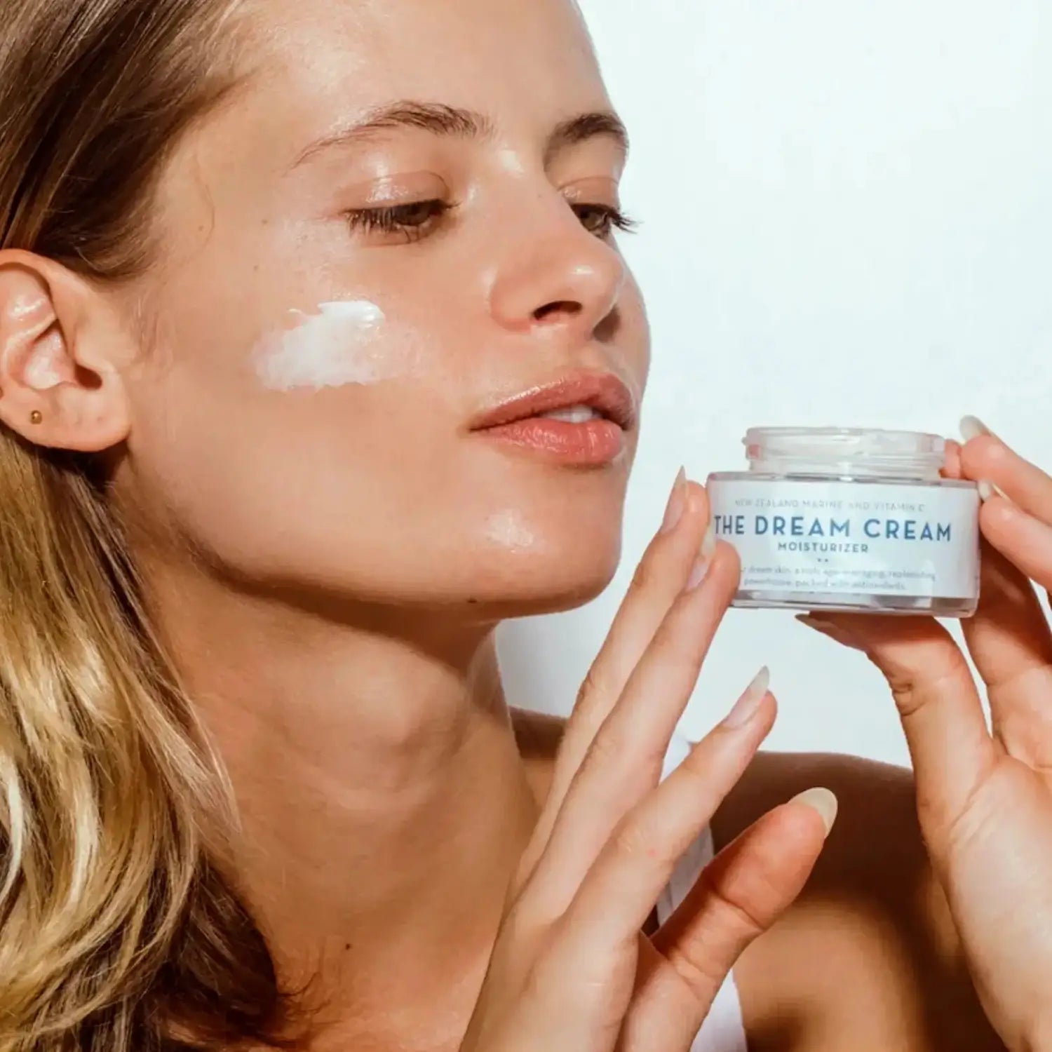 A woman applying The Organic Skin Co.'s Dream Cream Moisturizer to her cheek