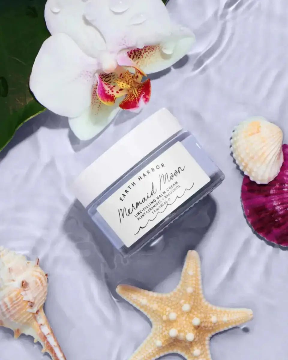 Earth Harbor Mermaid Moon Line Filling Balm Cream Jar next to Seashells and Flowers