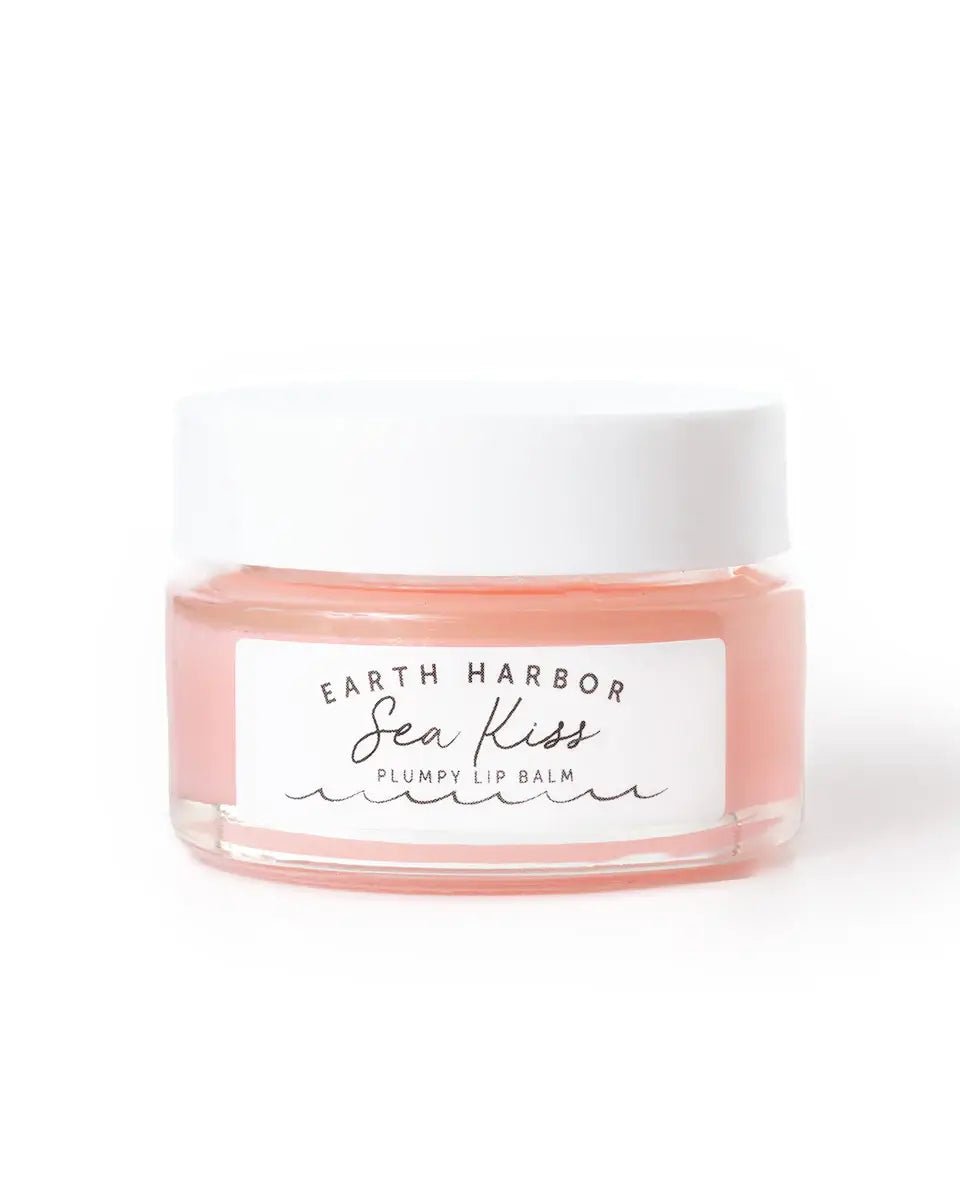 Earth Harbor SEA KISS organic lip plumping balm in a glass jar with a white lid, featuring a soft pink hue for hydration and smooth lips.