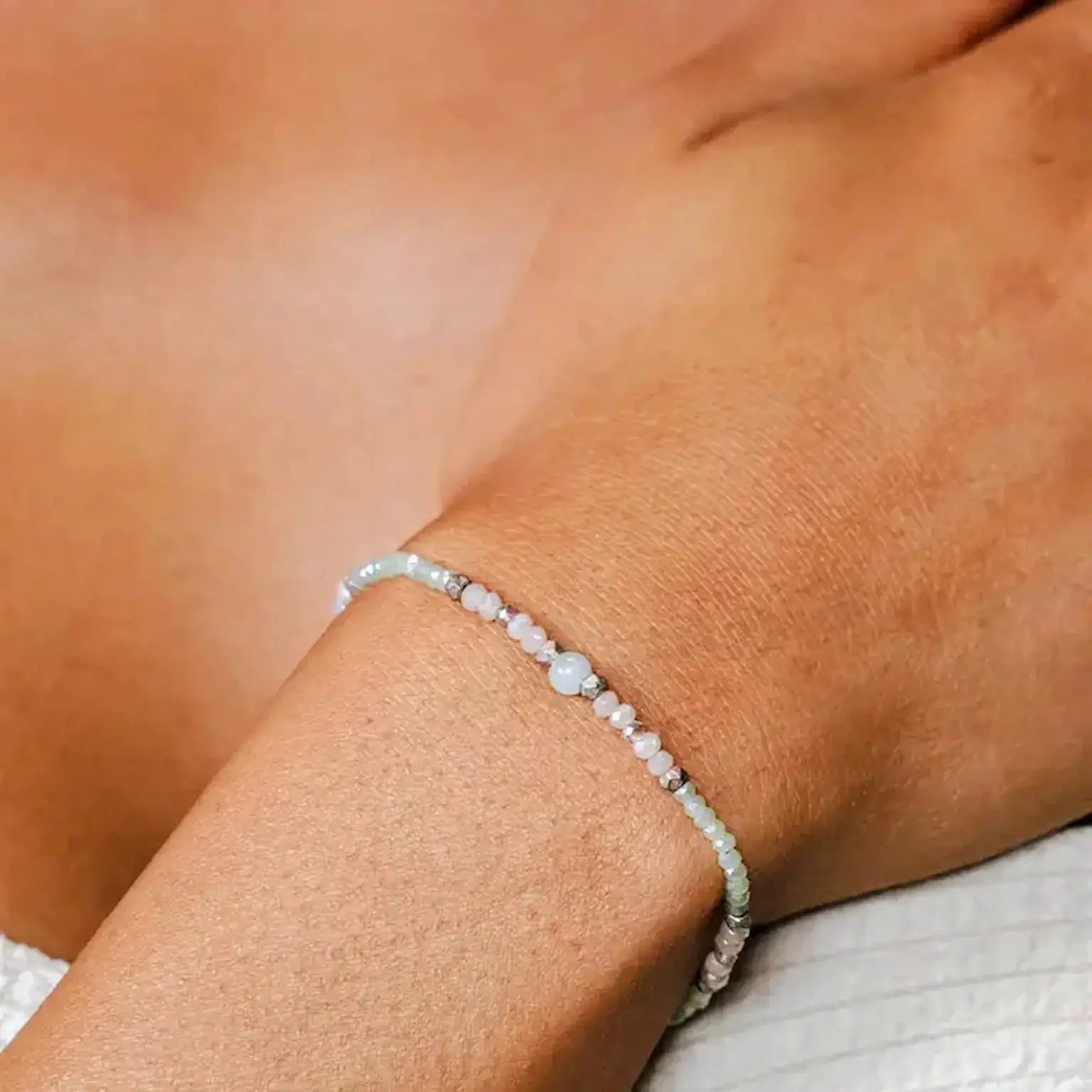 woman's wrist wearing a green amazonite stone bead bracelet surrounded by crystals