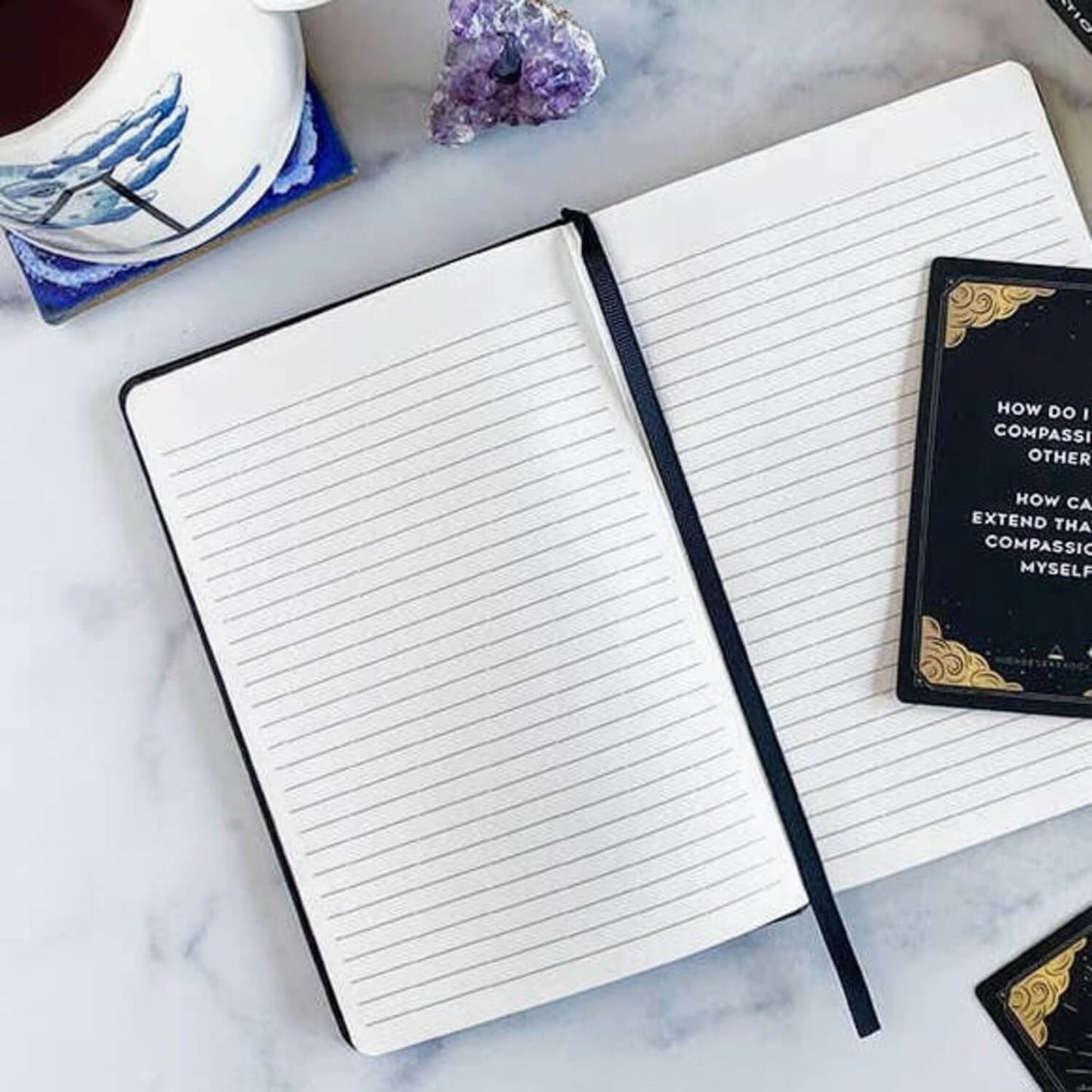 Open notebook with mediation cards on a marble surface with a cup of coffee and crystals.