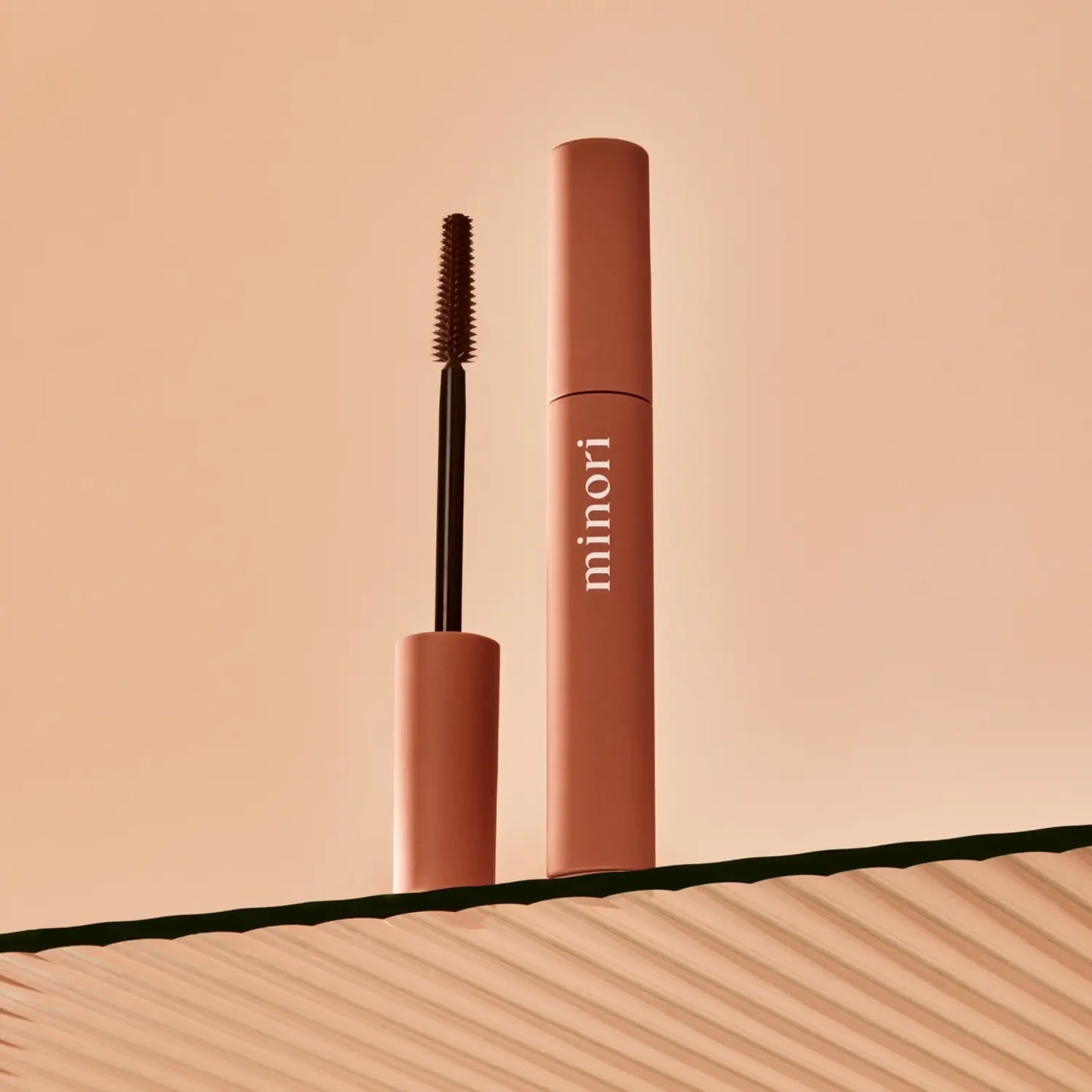a tube of minori mother of lashes mascara in brown shown with it's lengthening and defining bristle brush