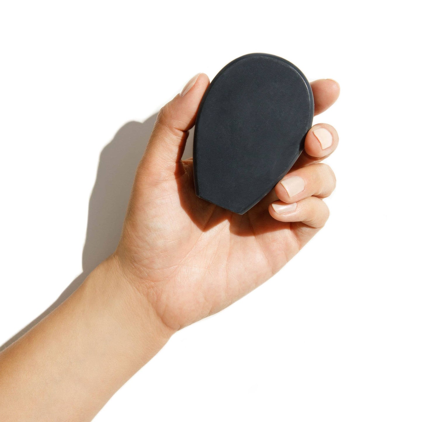 Hand holding a bar of nopalera noche clara charcoal soap against a white background