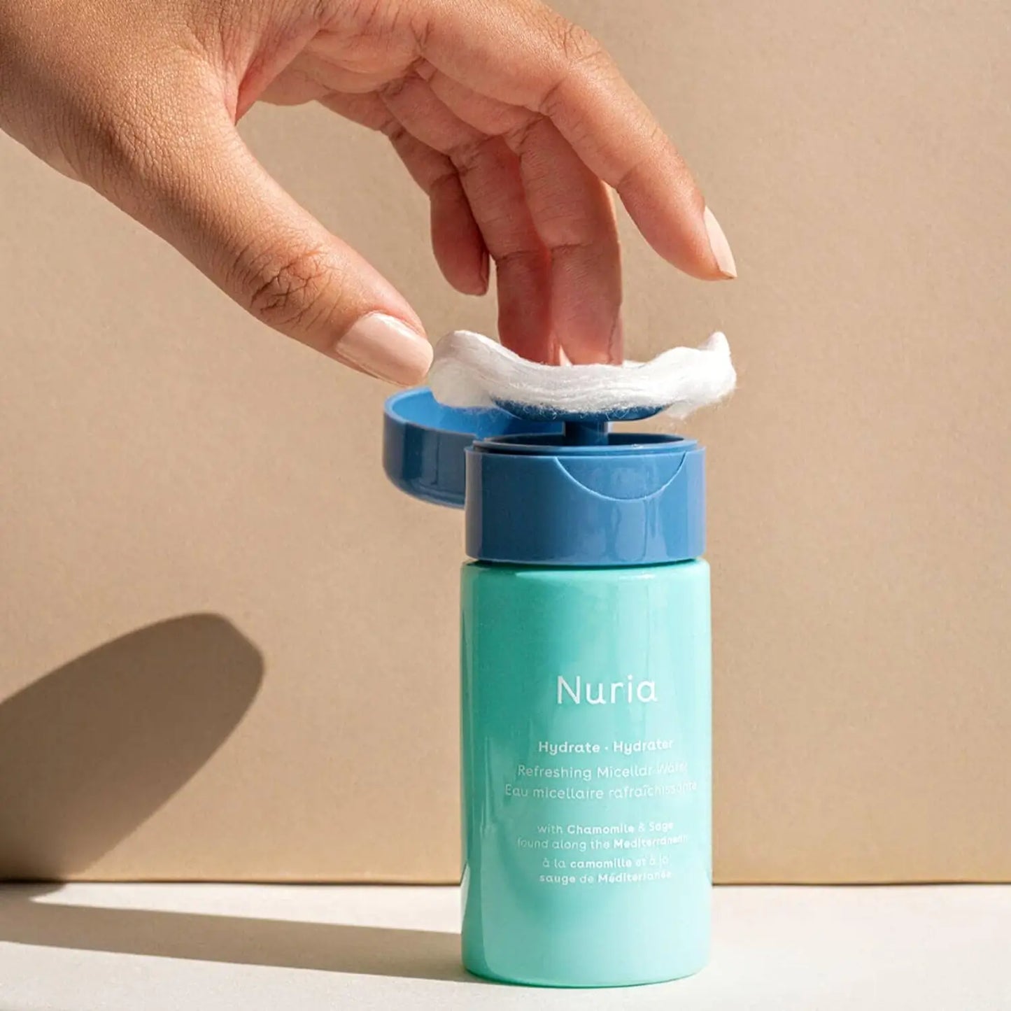 Hand holding a cotton pad to use nuria hydrate refreshing micellar water with built in pump dispenser