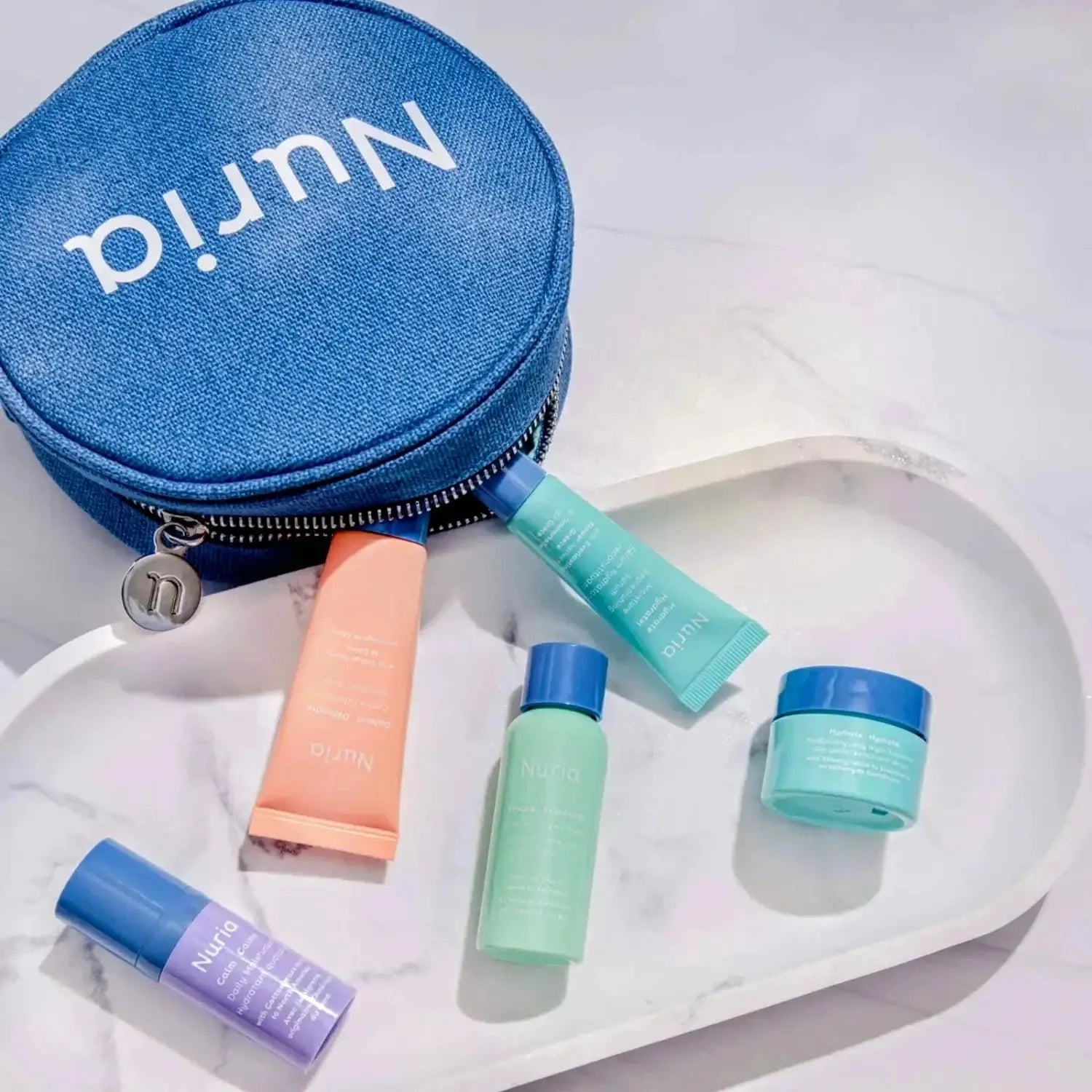 Nuria skincare products including travel size bottles and a round blue toiletry bag on a white background