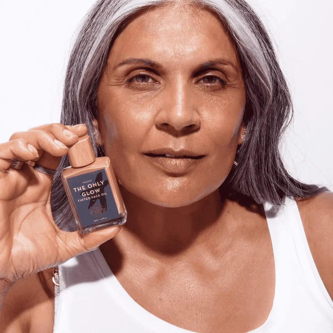 Mature woman holding The Only Glow Hydrating Organic Foundation Serum, showcasing its natural, radiant finish on her skin.