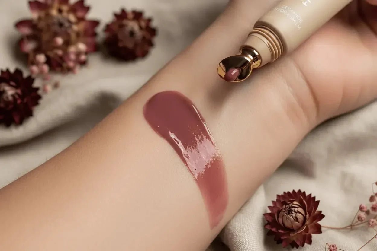 Color of the moment, a lip gloss swatch on an arm showing the rich plum shade and tube with gold tip applicator