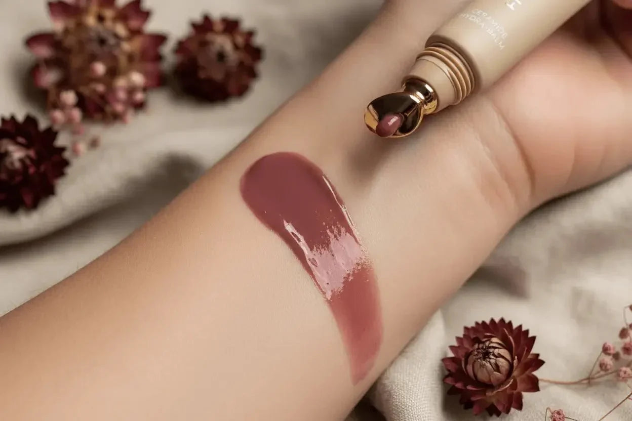 Color of the moment, a lip gloss swatch on an arm showing the rich plum shade and tube with gold tip applicator
