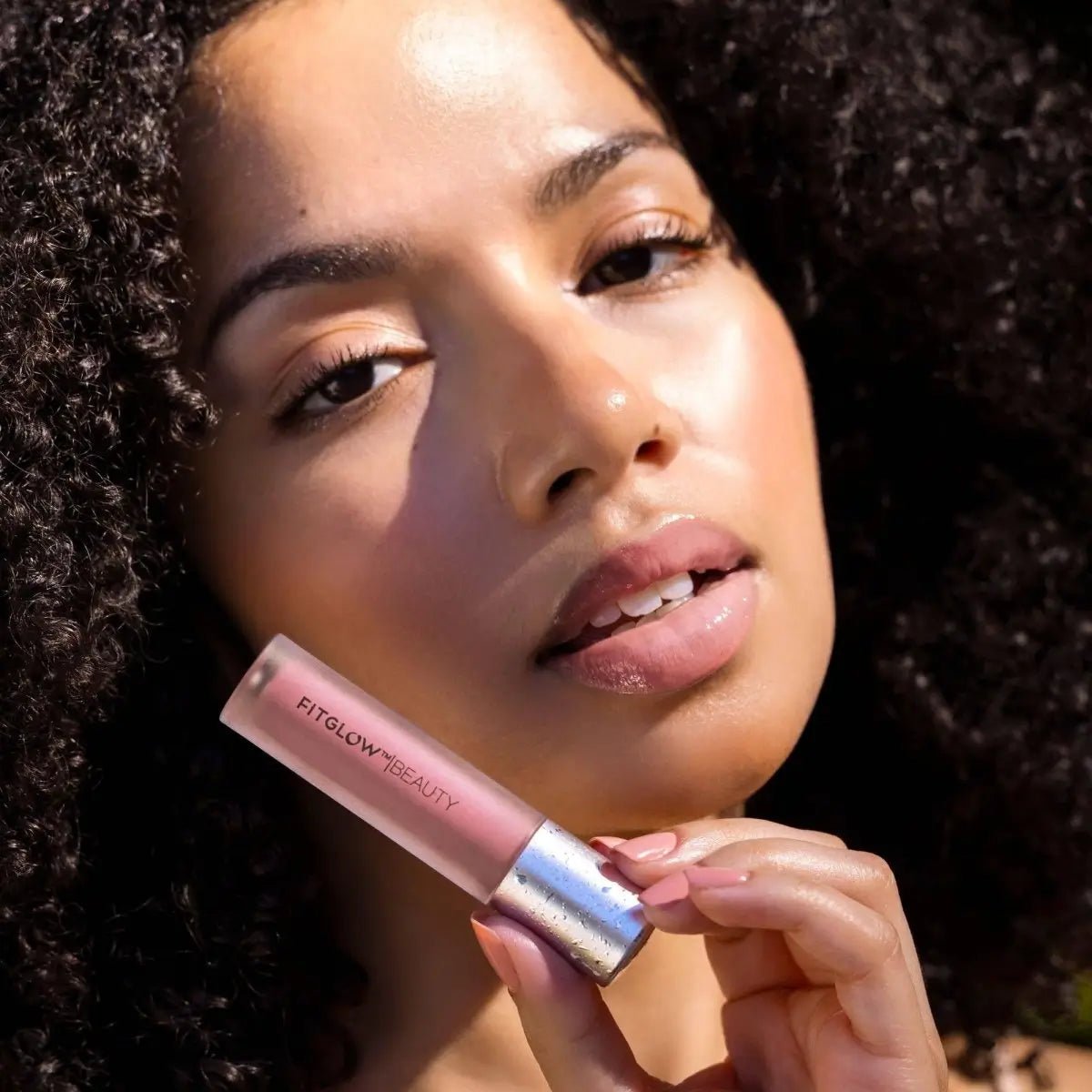 A woman holding a tube of Fitglow Beauty Lip Colour Serum in a pale pink shade. Shop Organic Cosmetics at Elle and Willow.