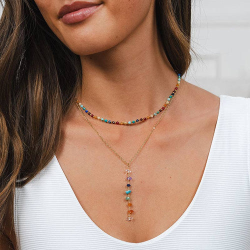 Model wearing 7 Chakras Healing Necklace layered with beaded choker, showcasing colorful raw gemstones on a gold chain.