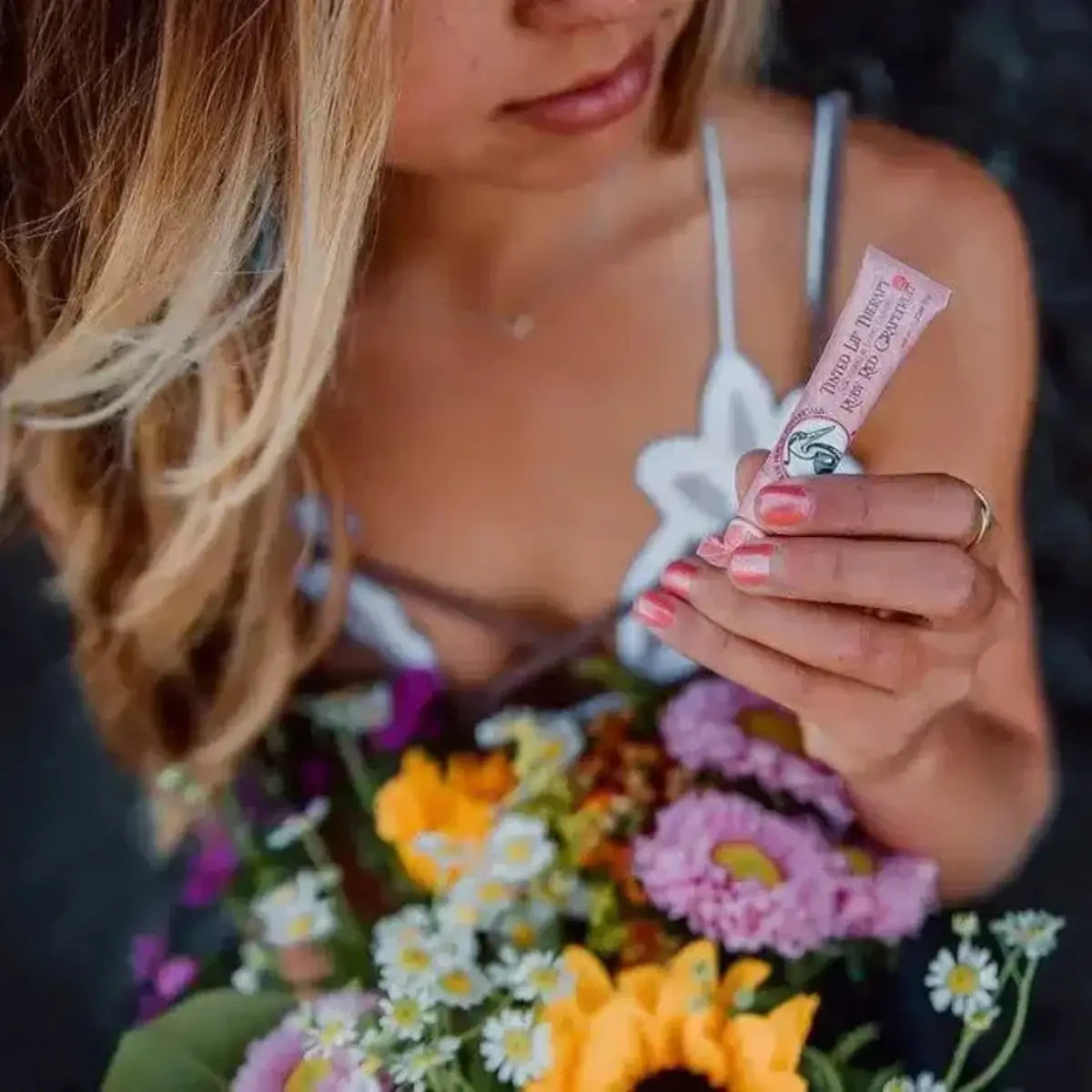 woman holding flowers and a tube of red lip balm