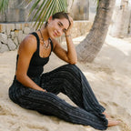 Woman wearing Striped Black Boho Harem Pants with Pockets by Lotus and Luna, styled for a beach day with a black tank top.