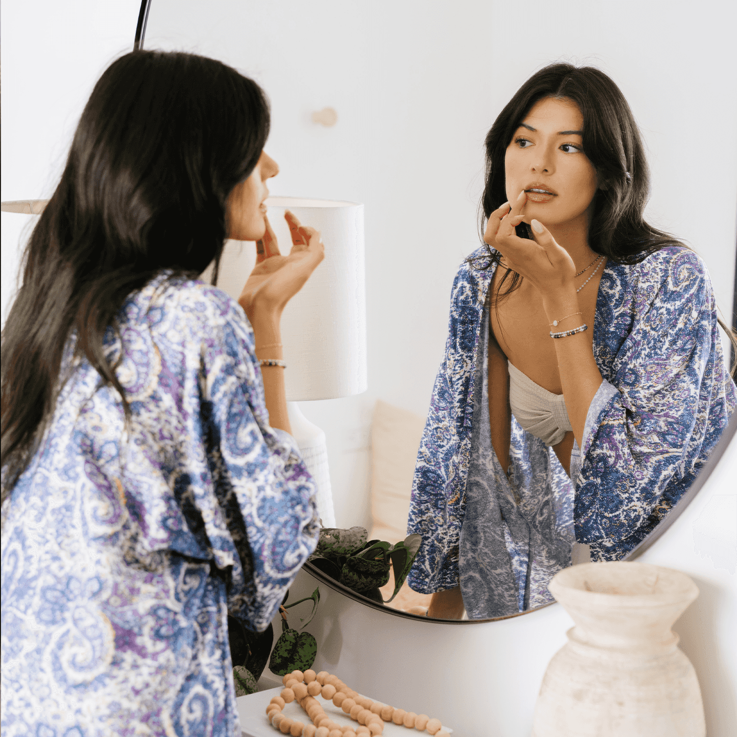 Lotus and Luna Beach Cover in Mumbai print, a lightweight handmade swim wrap with side slits, worn by woman applying lipstick in front of mirror.