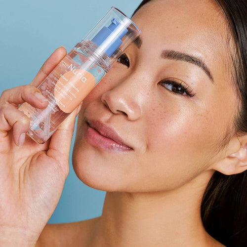 Woman holding Nuria Defend Skin Shielding Essence, a hydrating face essence with niacinamide beads and ginseng antioxidants.