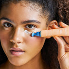 Model applying Nuria Eye Cream under her eye using the applicator, showcasing brightening and puffiness-reducing benefits.