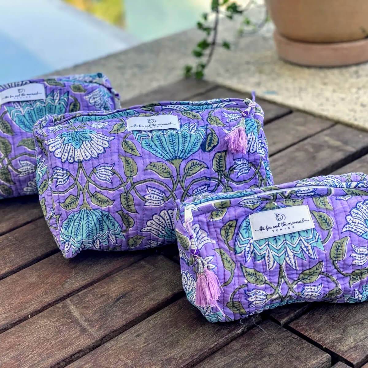 a set of three purple floral toiletry and cosmetics bags with zippers and decorative tassel pulls