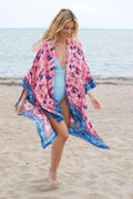a woman is walking on the beach wearing a pink and blue cover up