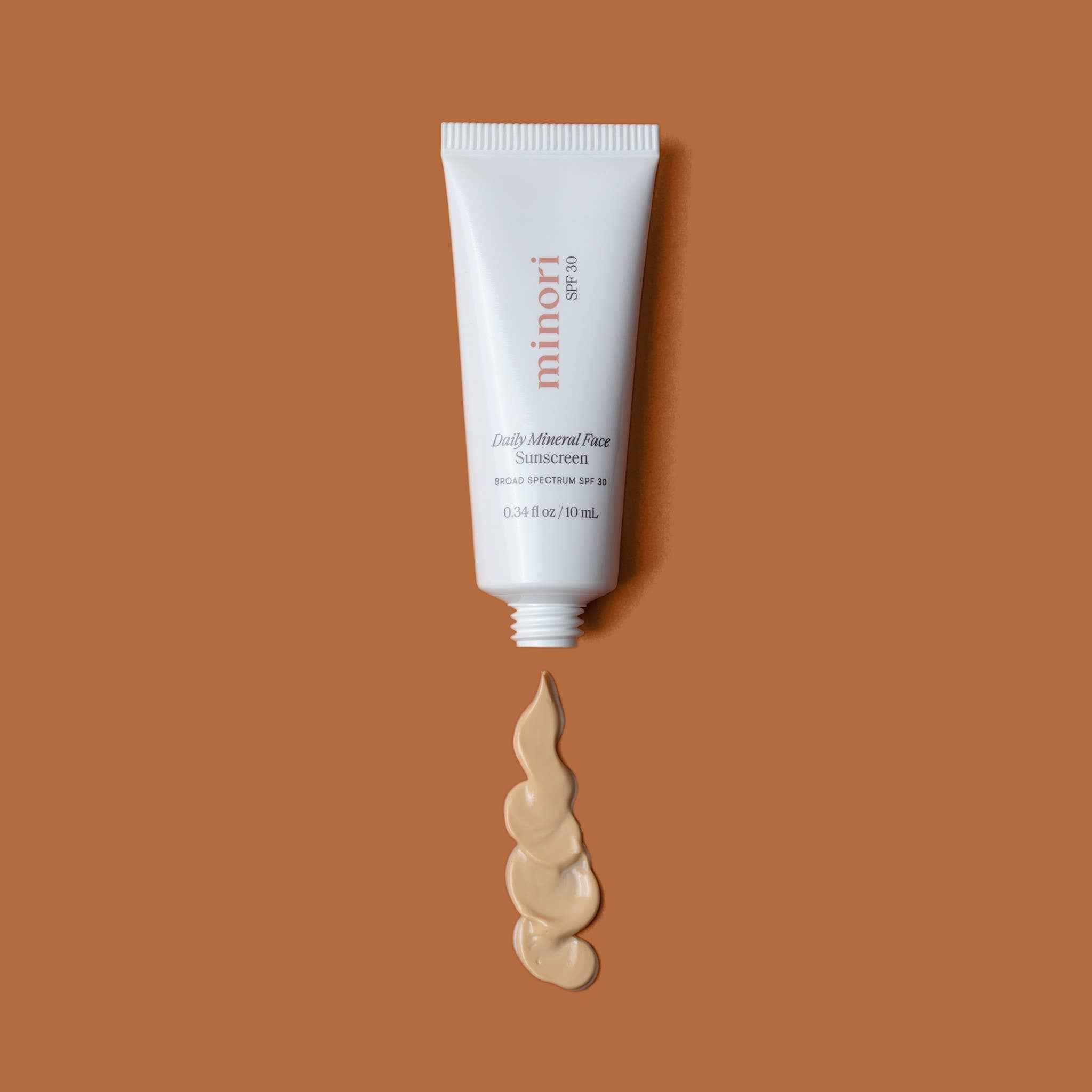 Minori Smoothing Face Primer with SPF 30 in a white tube, shown with creamy mineral sunscreen swatch on a brown background. Ideal for matte makeup base.