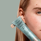 A woman holding a tube of The Organic Skin Co. Task Force Nine Aloe Calming Cream up to her face.