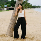 Black wide leg pants with pockets and a high-rise drawstring waist, styled with a white tank top on a beach. Comfortable boho lounge pants for casual wear.