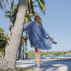 a woman next to a palm tree on the beach wearing a three quarter sleeve striped women's kimono cover up in blue.