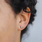 Woman wearing small blue turquoise earrings in a triangle shaped set in yellow gold.