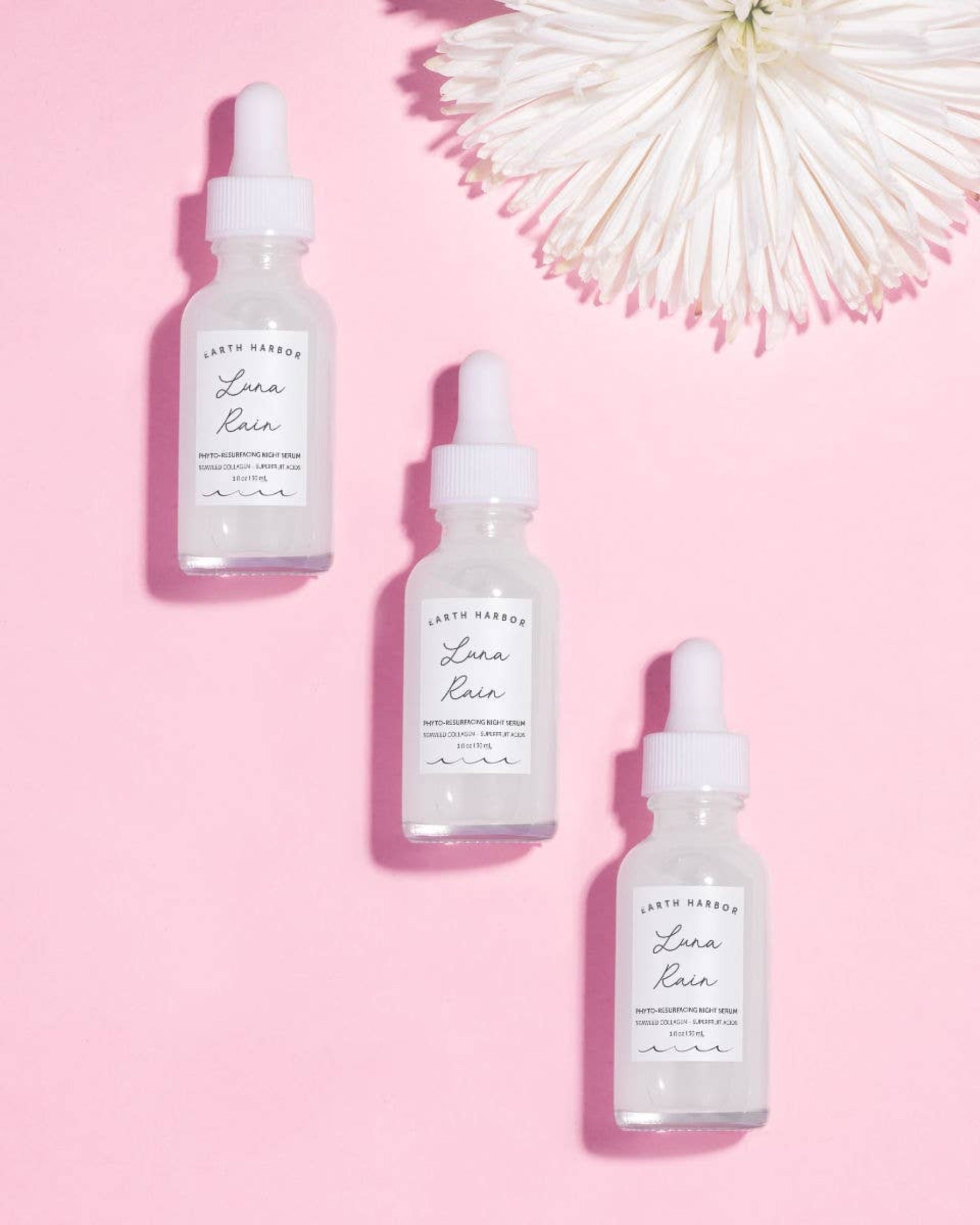 three 1 oz bottles of  earth harbor luna rain night serum on a pink background
