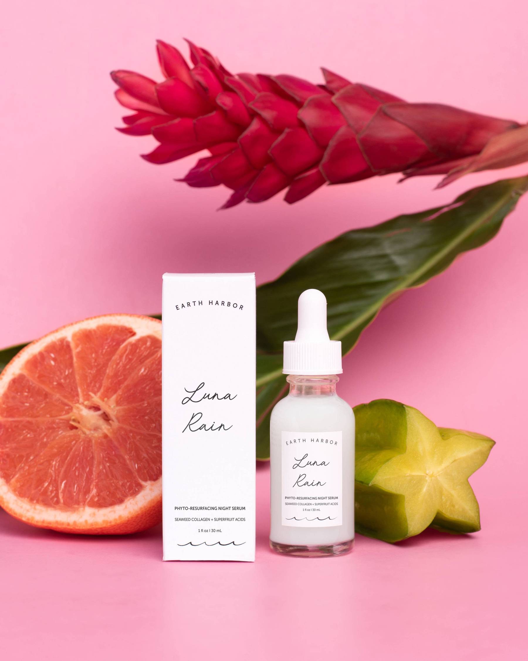a bottle of earth harbor luna rain night serum next to a grapefruit and a flower