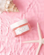 Sea Kiss lip balm jar placed on a pink textured surface with a seashell and starfish, emphasizing its ocean-inspired formula.