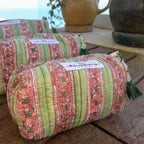 three fabric toiletry and cosmetic bags with zippered top and decorative tassel in a pink and green floral striped pattern.