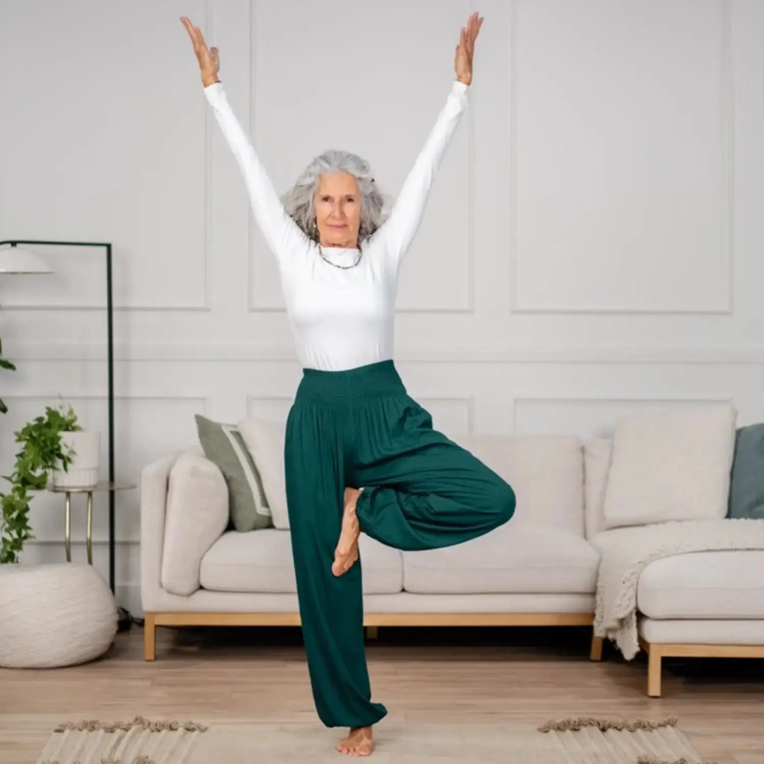 Forest Green Harem Pants with an elastic waistband, worn by a woman practicing yoga in a stylish living room. Perfect for comfort and flexibility.
