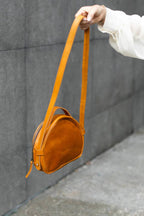 a person holding a brown leather crossbody bag on an adjustable shoulder strap