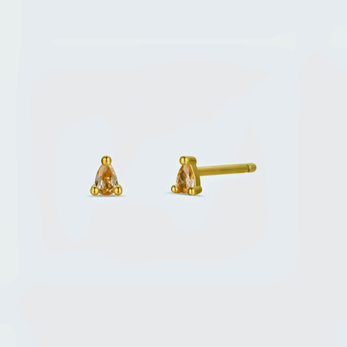 Gold stud earrings with pink champagne gemstones on a light gray background