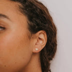 a close up of a person wearing a pair of lotus flower yellow gold huggie earrings