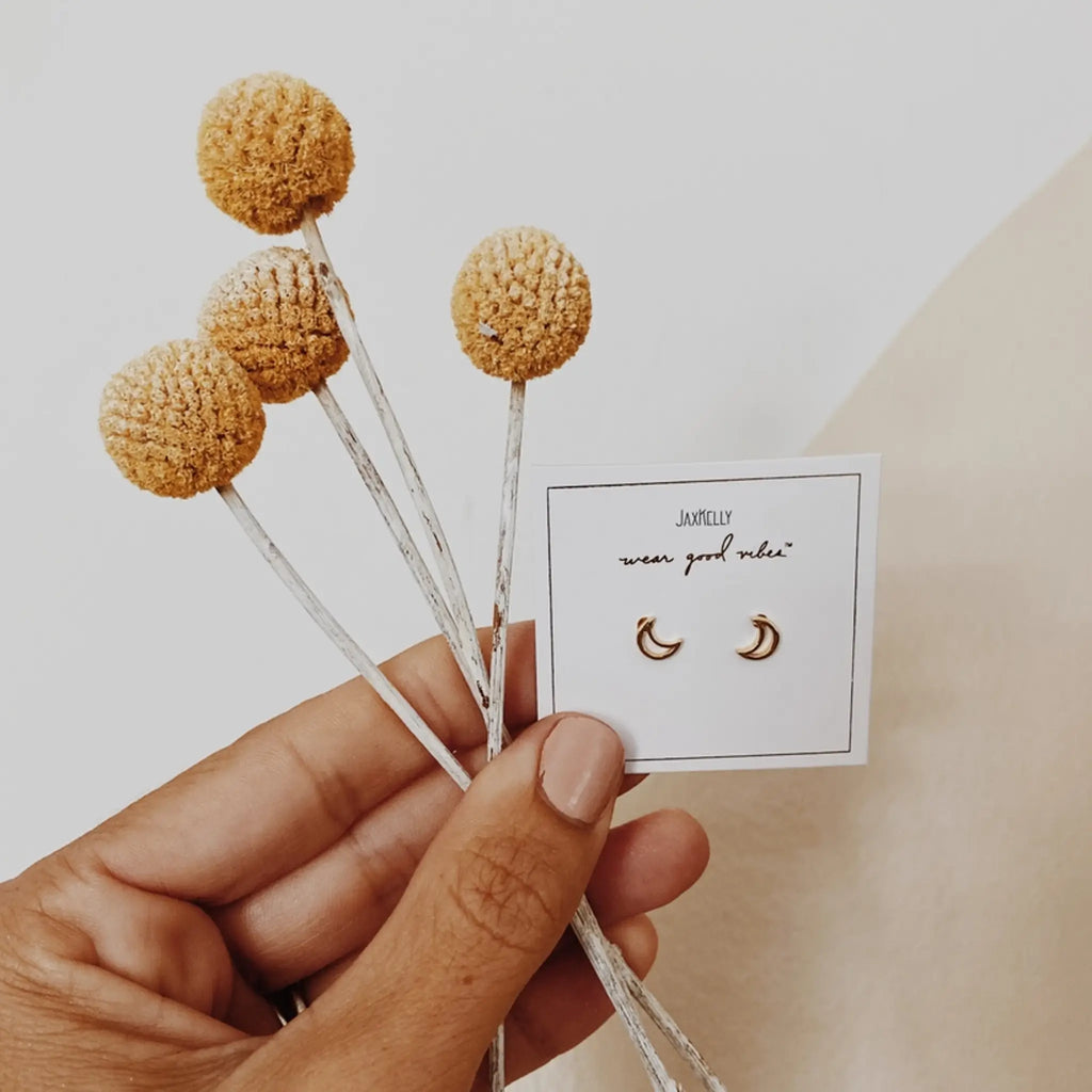 a hand holding dried flowers and a JaxKelly jewelry card with moon earrings