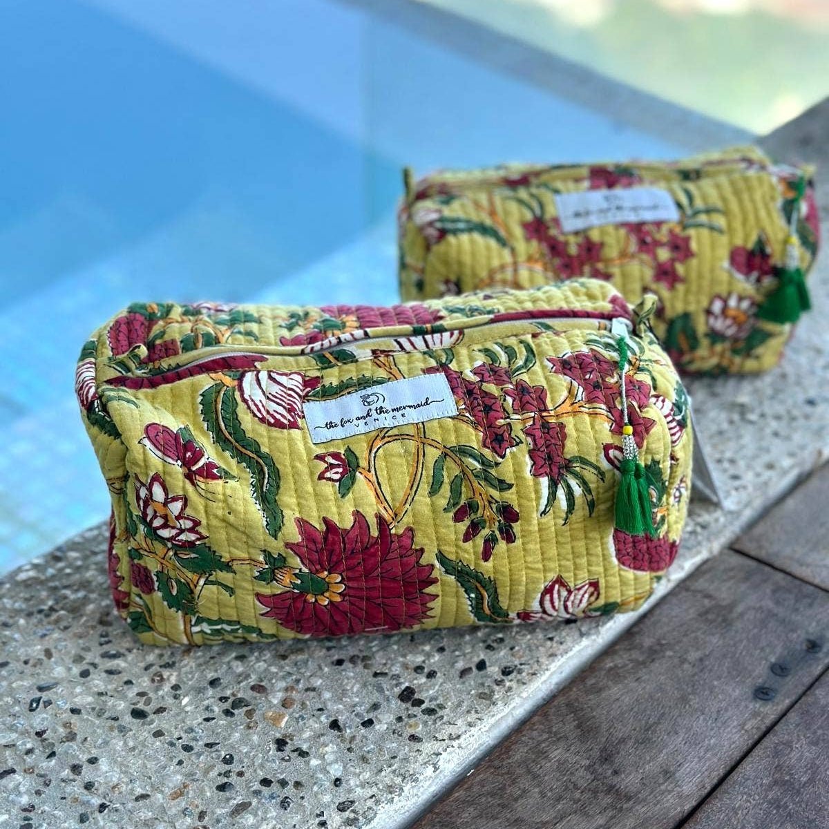 Two floral-patterned cosmetic pouches on a textured surface with a blurred outdoor background