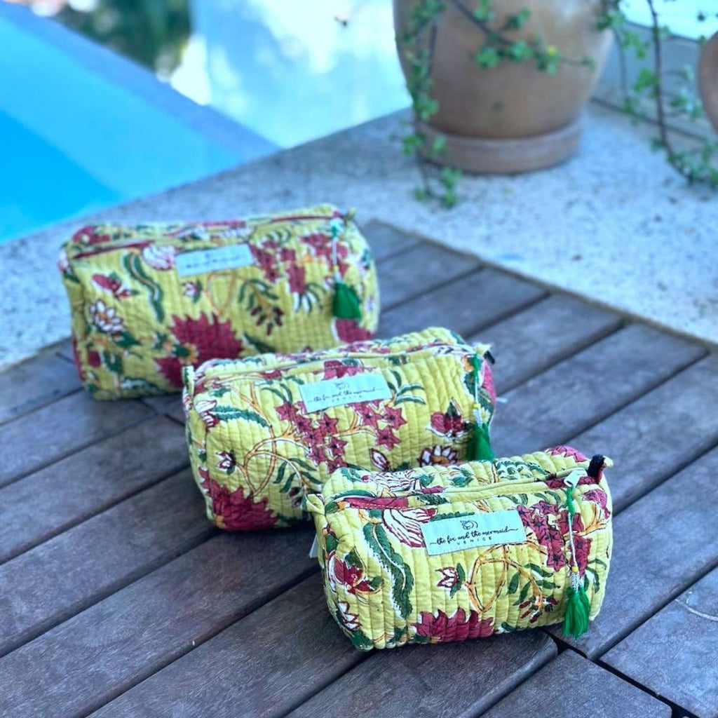 Three floral-patterned handmade cosmetic bags on a wooden surface with a blurred outdoor background