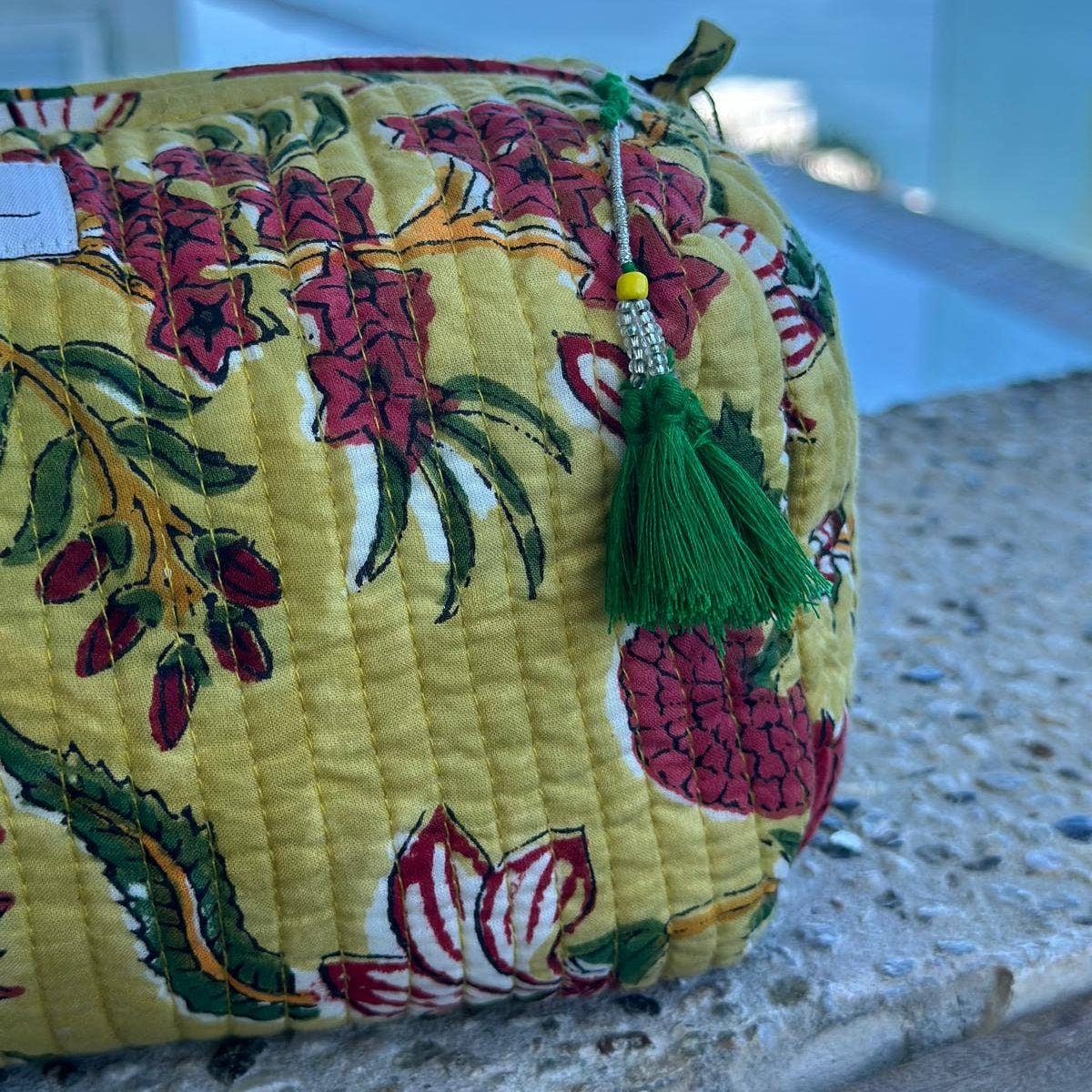 Yellow with floral pattern cosmetic bag with green tassel top zipper pull on a textured surface