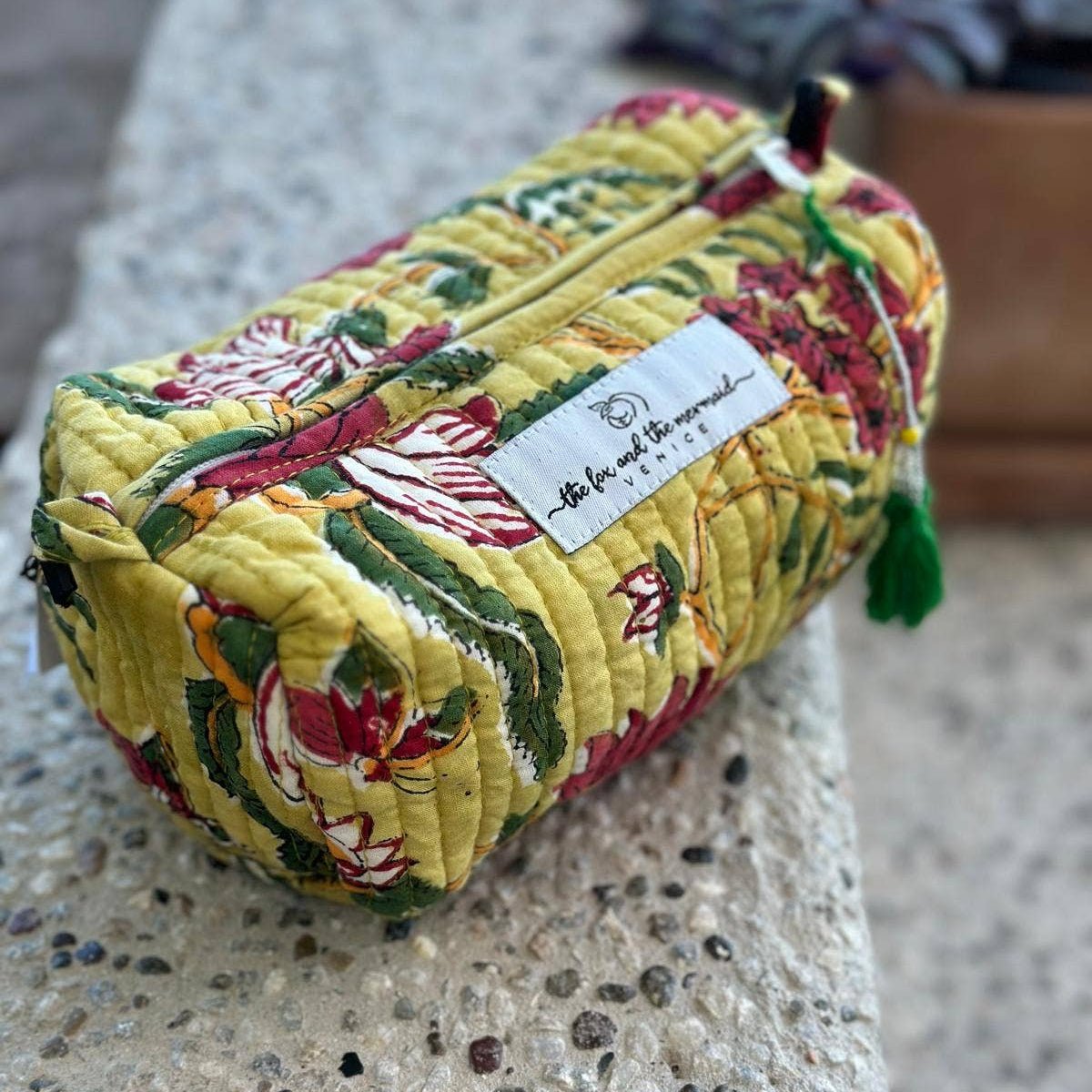 Floral-patterned fabric cosmetic bag with The Fox and the Mermaid brand label on a textured surface