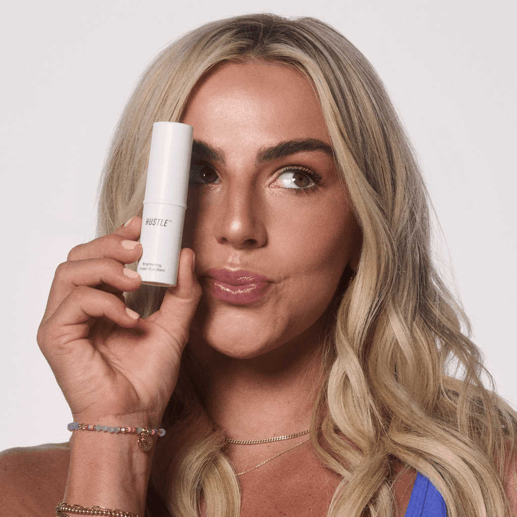 Cavinder twin holding a tube of brightening under-eye balm from hustle beauty with a neutral background
