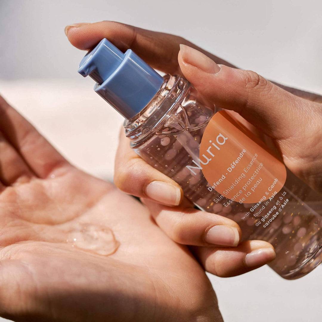 Nuria Defend Skin Shielding Essence Mini face serum dispensed onto hand, showcasing hydrating antioxidant-rich formula with Niacinamide beads.