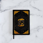 Black notebook with gold design  for intention and mindfulness on a marble surface