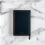 back view of intention and minfulness journal black notebook with gold trim on a marble surface