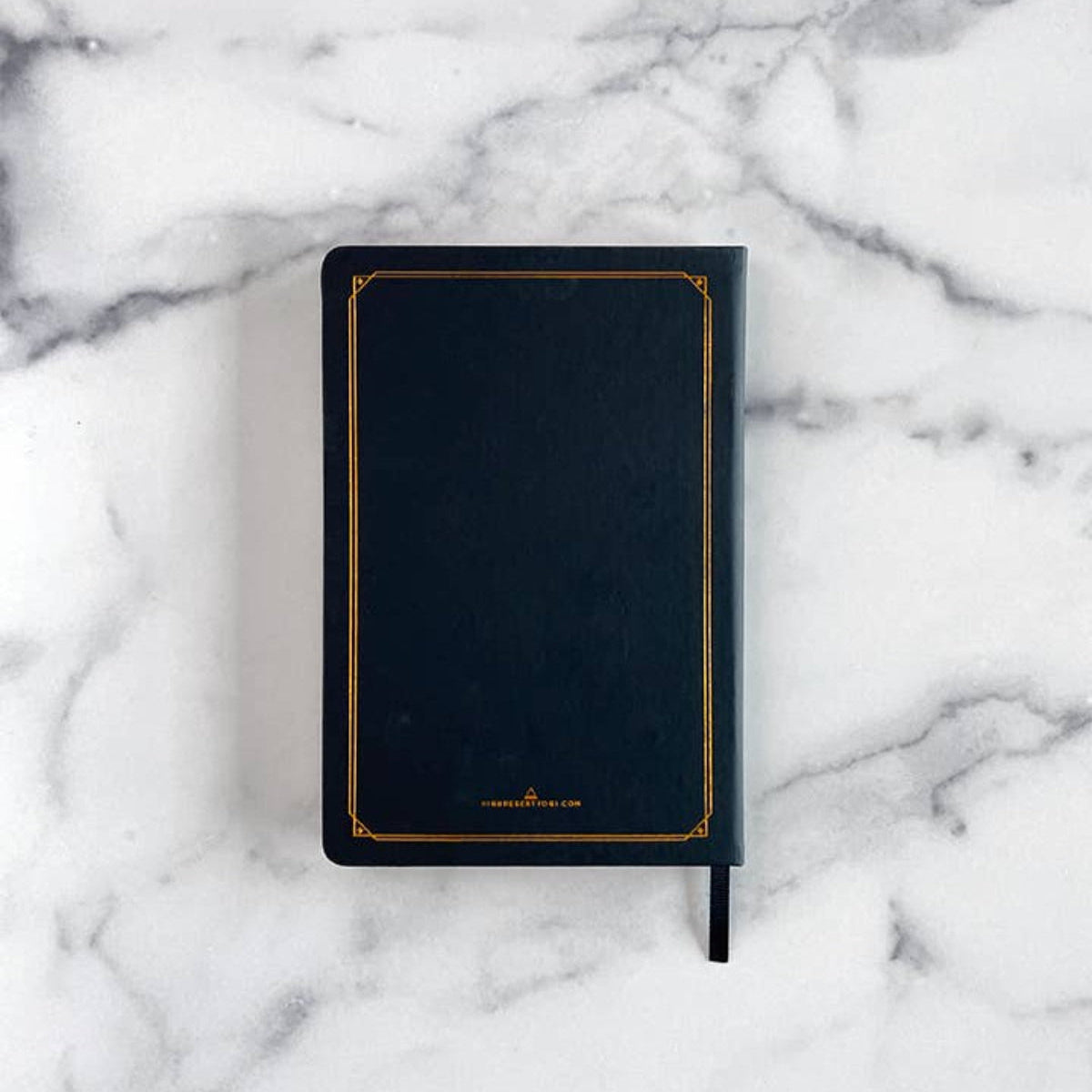back view of intention and minfulness journal black notebook with gold trim on a marble surface